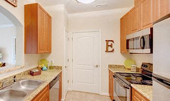 Galley-style kitchen with upgraded granite countertops and stainless steel appliances; open to living room